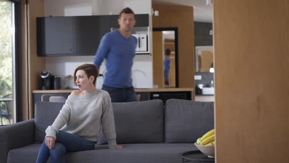 Slim Woman Sitting on Couch Standing Up Walking Away As Aggressive Angry Man Shouting Gesturing