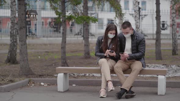 A Man and a Woman Wear Protective Masks on the Street Online Using a Smartphone During the Pandemic