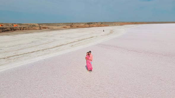 Slow Motion Aerial Footage of Affectionate Couple Gently Embracing on White Salty Coast of Pink Lake