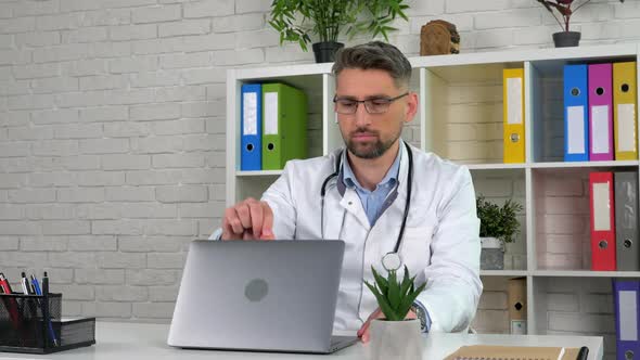 Remote doctor wears white medical coat in hospital office opens using laptop