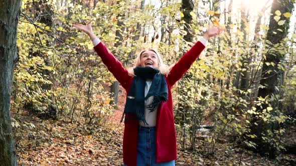 SLOWMOTION Young beautiful woman throwing leaves in the air amidst thee orange brown autumn forest w