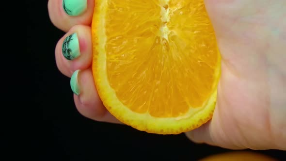 Woman's Hand Squeezes Fresh Juice From an Orange in Slow Mo on Black Background