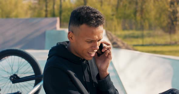 A Darkskinned Young Boy Sits in a Skatepark in the Afternoon a Bmx Next to