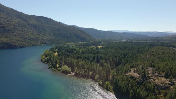 Aerial dolly in of turquoise Epuyen lake between pine trees and mountains, Patagonia Argentina