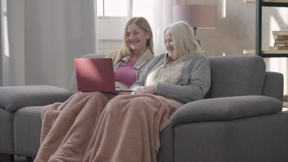 Wide Shot Portrait of Two Laughing Senior Caucasian Women Surfing Social Media on Laptop Talking