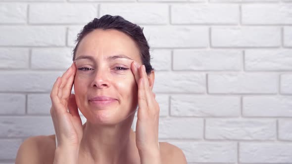 The woman examines her face in the mirror. 