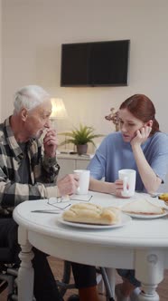 Grandfather in a Wheelchair Chatting with a Young Woman Over a Cup of Coffee