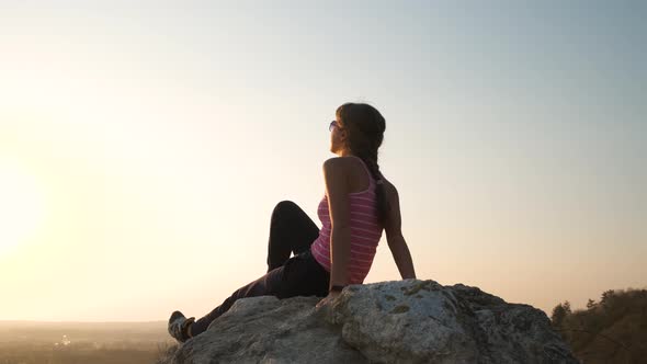 Young relaxed woman sitting outdoors on a big stone enjoying warm summer day. Girl meditating