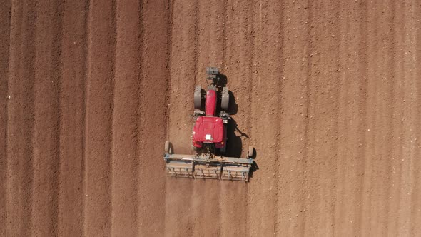 Red tractor flattening a field for seeding, Drone follow footage.