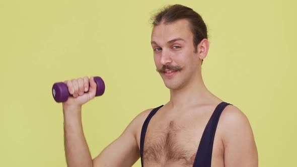 Sporty Man in Overalls Making Exercises with Dumbbell Puting It Up Smiling in Slow Motion