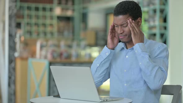 Young African Man with Laptop Having Headache in Cafe