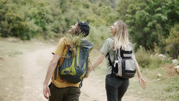 A Happy Couple Backpackers Walking By Forest's Path and Holding Hands