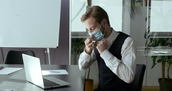 Businessman Freelancer in Face Medical Mask Sitting at Table Messaging Online on Covid-19 Lockdown