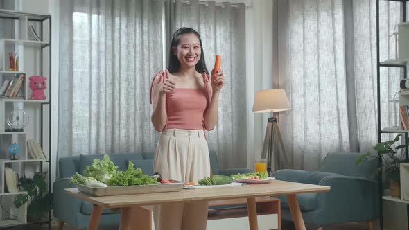 Smiling Asian Woman Holding A Knife And Slicing Carrot Before Showing Thumbs Up Gesture To Camera