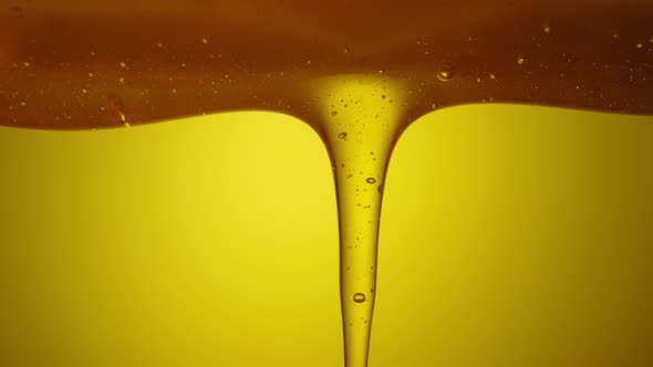 Drops of Thick Golden Honey Flowing Down on a Yellow Background