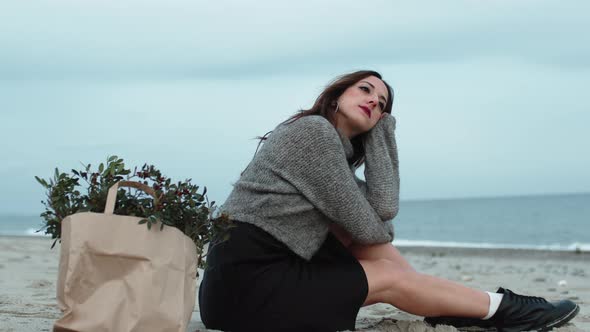 Young Girl Sitting on the Beach Near the Sea with a Bunch of Leaves