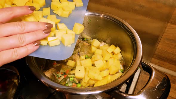 Female hands are putting freshly chopped potatoes into a steaming hot stew. Homemade cooking. Cookin