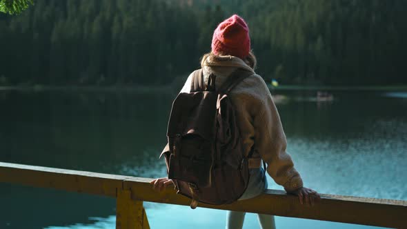 Rear View Hiker Woman Sits on Wooden Pier By Beautiful Mountain Lake and Enjoys Amazing Calm Forest