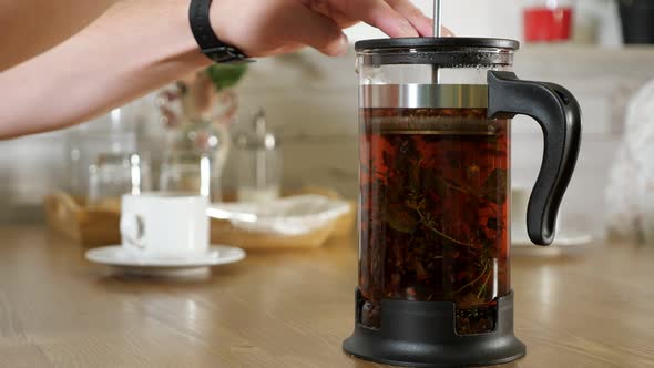 Man Brews Black Tea in French Press at Wooden Table Closeup