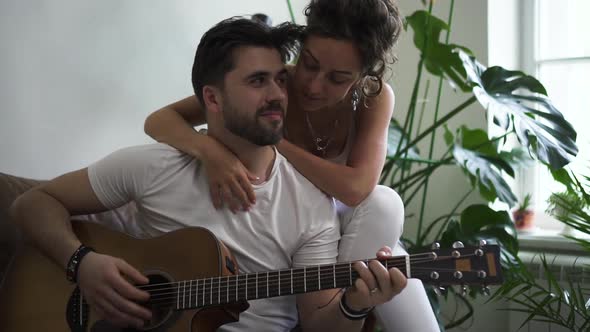 Young Woman and Man Playing Guitar While Sitting on Sofa in Modern Apartment Spbd