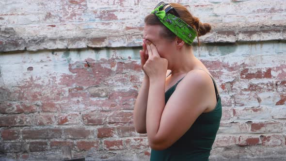 Woman with allergy symptom scratching red eyes on brick background. Sick stressed young girl  face