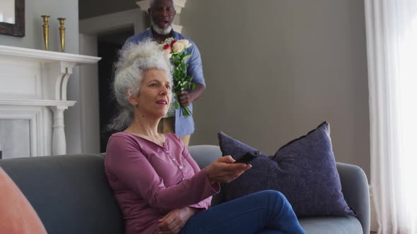 African american senior man giving flower bouquet to his wife at home