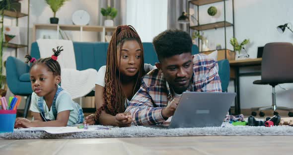 Afro American Parents Using Laptop while Daughter Drawing