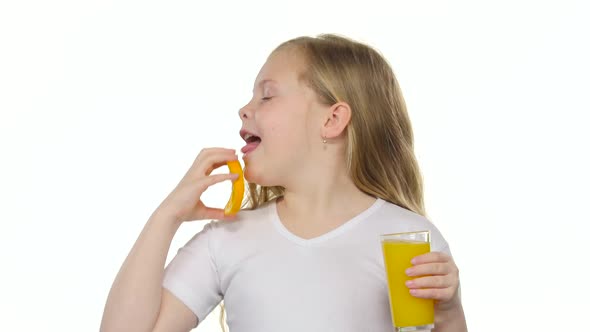 Little Girl Holds an Orange Slice and Licks It and Drinks Orange Juice. White Background