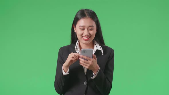 An Asian Business Woman Enjoy Using Mobile Phone While Standing On Green Screen In The Studio