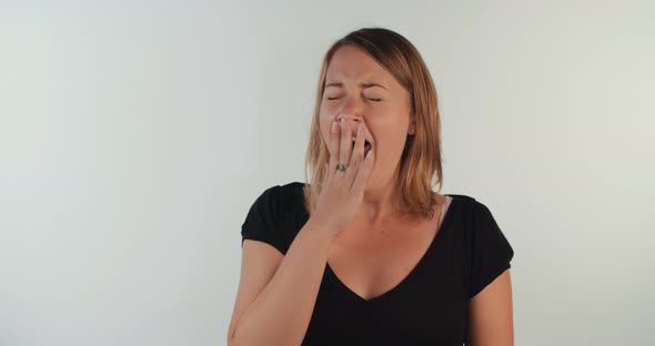 Young blond woman yawning in slow motion on white background