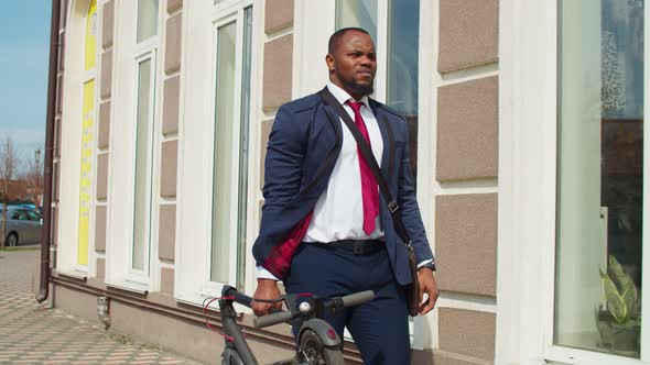 Black Male Entrepreneur Carrying Electric Scooter Along Street