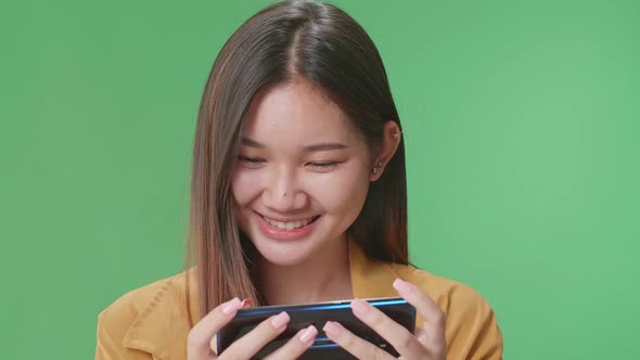 Asian Woman Looking At The Phone Screen And Holding It In Her Hands In Green Screen Studio