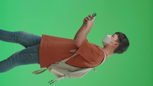 Asian Boy Student Wearing A Mask, Using Mobile Phone While Walking To School On Green Screen