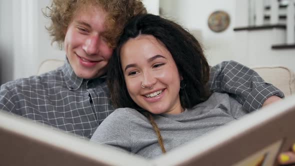 Attractive Amorated Happy Young Couple Looking Photo Album on the Couch in the Living-Room