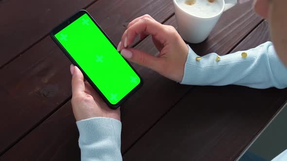 Womans Hand Use Green Screen Smartphone for Online Shopping at Cafe Table with Coffee Cup