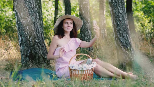 Picnic Time. Young Beautiful Girl with Round Hat Sitting on the Plaid and Posing for Selfies