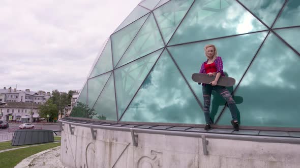 Portrait of Pretty Teenage Girl Posing with Skateboard in Front of Glass Building