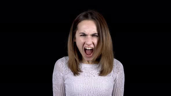 A Young Woman Shows Emotions of Anger on Her Face. Woman Screams in Anger on a Black Background.