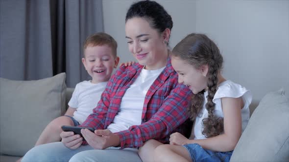 Mother Playing with Children at Home Relaxing Use a Smartphone Cuddling Sit on Sofa Daughter and Son