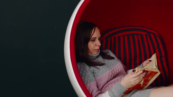 Young Woman Reads Old Book Sitting in Ball Chair