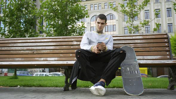 Handsome Guy Sitting on the Bench in the Park Listening To Music on His Cellphone