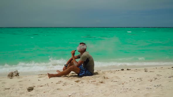 A Man Smokes a Vape on a Tropical Beach