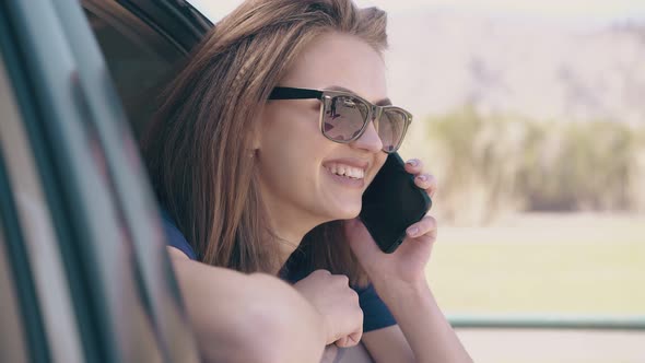 Smiling Lady with Phone Looks Out of Open Automobile Window