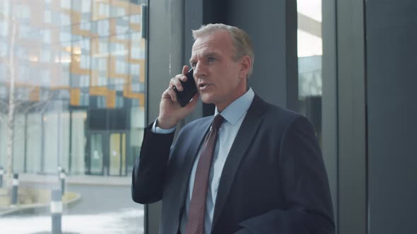 Middle-Aged Businessman Talking on Mobile in Hallway of Office Building