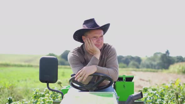 Handsome Farmer in a Hat Sits on a Mini Tractor Outdoors in the Garden