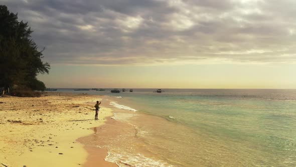 One man fishing on relaxing coast beach break by blue water with white sandy background of Lombok is