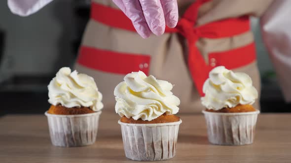 Pastry Chef Sprinkles Muffins with Cream in Paper Cups with Chocolate Crumb