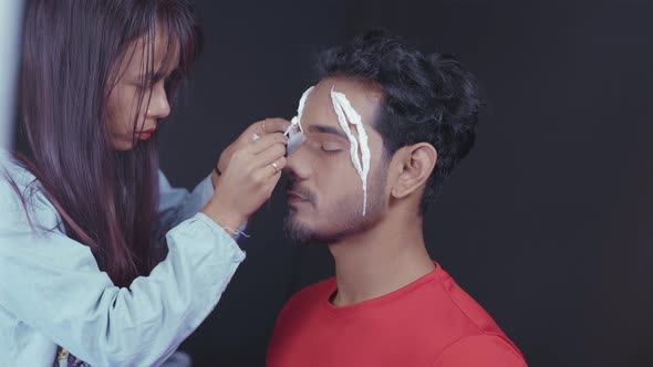 Professional make up artist putting white prosthetic insert on man's face to make a Halloween mask