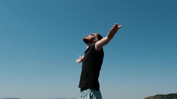 Man on the Top Om Hill and Spread His Arms in Different Directions. Young Bearded Man in Black 