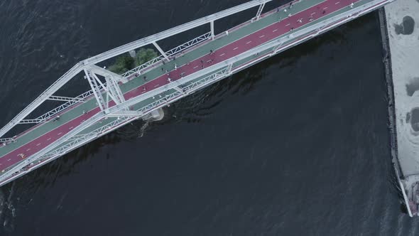 People Walk on a Footbridge Over a River with a Cargo Barge Filled with Sand